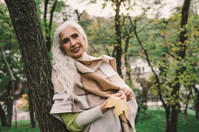 Portrait of woman holding autumn leaf standing at park