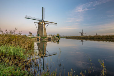 Traditional windmill by lake against sky