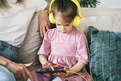 Little girl in yellow headphones sits on a sofa with a phone.