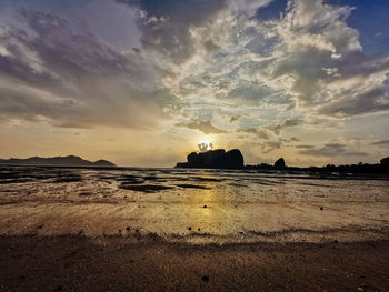 Silhouette land on beach against sky during sunset