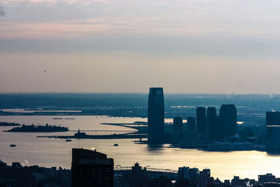 Modern buildings by sea against sky during sunset