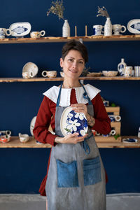 Successful ceramics studio owner posing with handmade plate at workplace