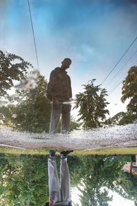 Rear view of man standing by tree against sky