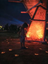 Rear view of woman standing by fire at night