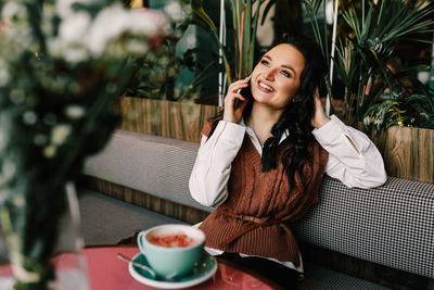 Smiling young woman using phone while sitting on table