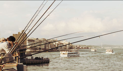 People with fishing rod by sea against sky in city