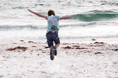 Full length rear view of boy jumping on shore