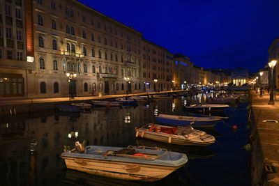 Boats moored in canal by illuminated buildings in city at night