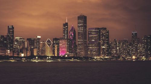 Illuminated modern buildings in city against sky at night