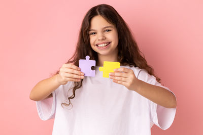 Portrait of young woman holding piggy bank against pink background