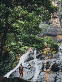 Man standing on rock against waterfall, beautified by its trees and natural rocks