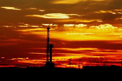 Silhouette tower and buildings against orange sky