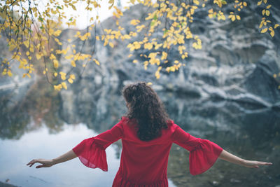 Beautiful curly hair woman in a red dress at the lake with arms stretched out