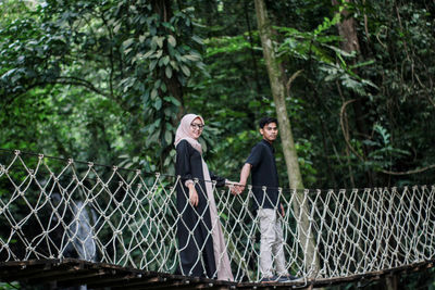 Portrait of couple standing on footbridge in forest