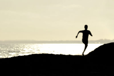 Silhouette man standing on beach against sky during sunset