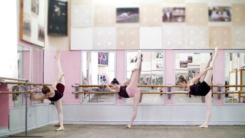 In dancing hall, young ballerinas in black leotards are stretching, standing near barre