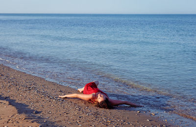 Full length of woman lying down on beach against sky