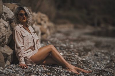 Full length of woman sitting on pebbles at beach