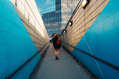 Rear view of woman walking on pedestrian walkway amidst wall