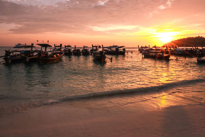 Boats moored in sea against sky during sunset