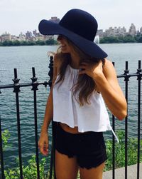 Young woman wearing hat while standing against river