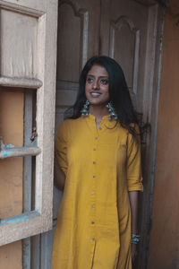 Portrait of smiling young woman standing against yellow wall