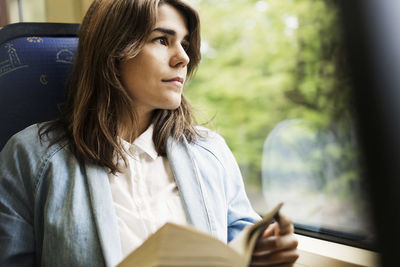 Young woman holding book while looking through tram window