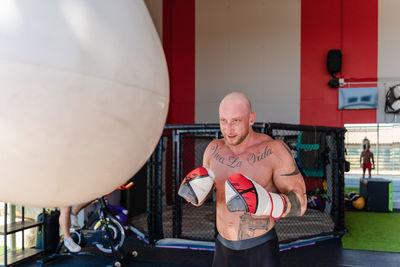 Determined male boxer in boxing gloves punching heavy bag during intense workout in gym