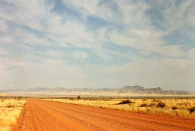 Road passing through field against cloudy sky