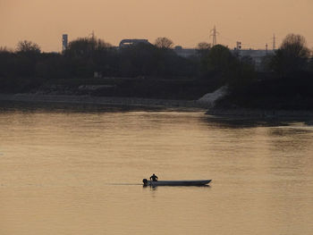 People in boat on lake against sky during sunset