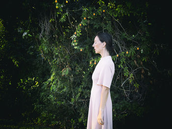 Woman in short pink dress in front of a hedge iv