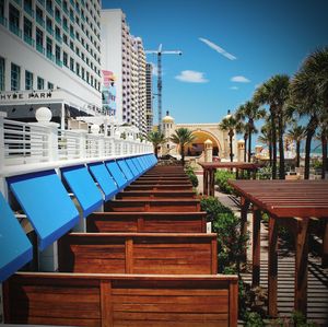 Empty chairs by palm trees and buildings against blue sky