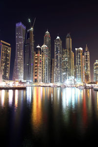 Low angle view of illuminated city reflecting in bay against clear sky