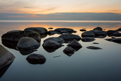 Rocks in sea against sky at sunset