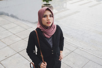 Portrait of beautiful young woman standing on footpath