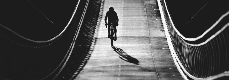 Silhouette man cycling on bridge