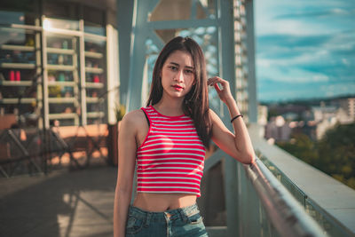 Portrait of young woman standing against railing