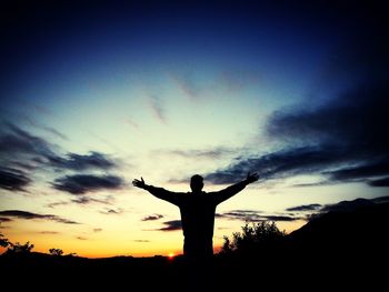 Silhouette man standing with arms outstretched against sky during sunset