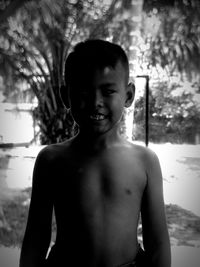 Portrait of shirtless boy standing against tree