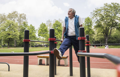 Smiling active senior man exercising on gymnastics bar at park