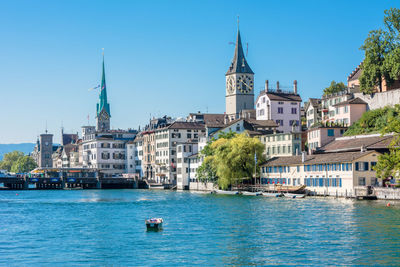 Sailboats in canal by buildings against blue sky