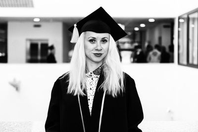 Female blonde college or high school graduate confidently wearing black cap and gown at graduation