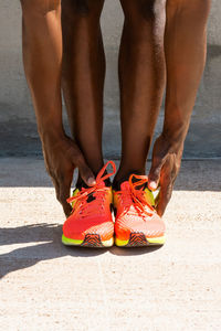 Crop unrecognizable african american male athlete in vivid sneakers doing forward bend and stretching legs during training on sunny day in city