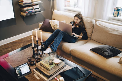 High angle view of girl using mobile phone and laptop while sitting on sofa