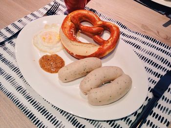 High angle view of fresh weisswurst and pretzel with poached egg in plate served on table