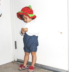 Full length of cute girl in hat standing against wall