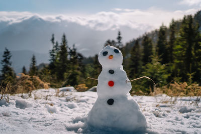 Close-up of snowman on mountain against trees and mountains during winter