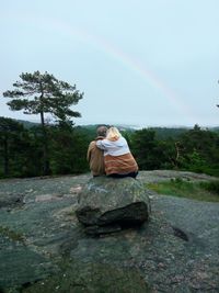 Woman standing on rock by road against rainbow in sky
