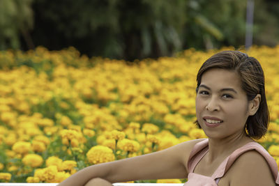 Portrait of smiling woman sitting against yellow flowers