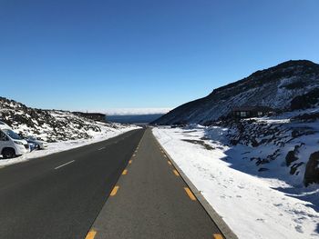 Road amidst snowcapped mountains against clear sky